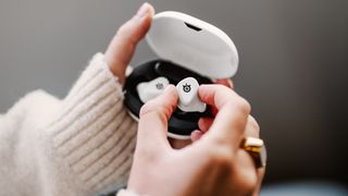 SteelSeries Arctis GameBuds in white with a lady's hand removing one bud from the box