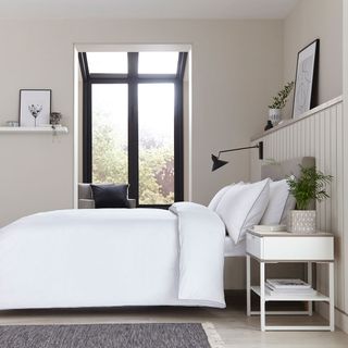 bedroom with white bedding white walls and potted plant