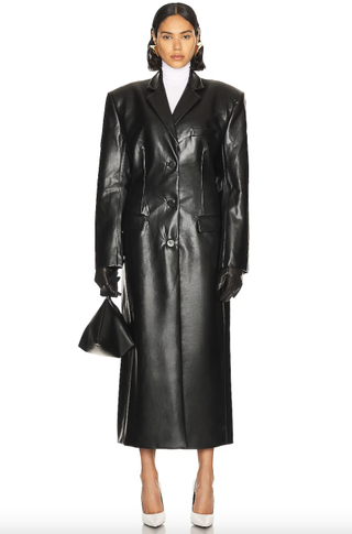 a model wears a leather trench coat in front of a plain backdrop