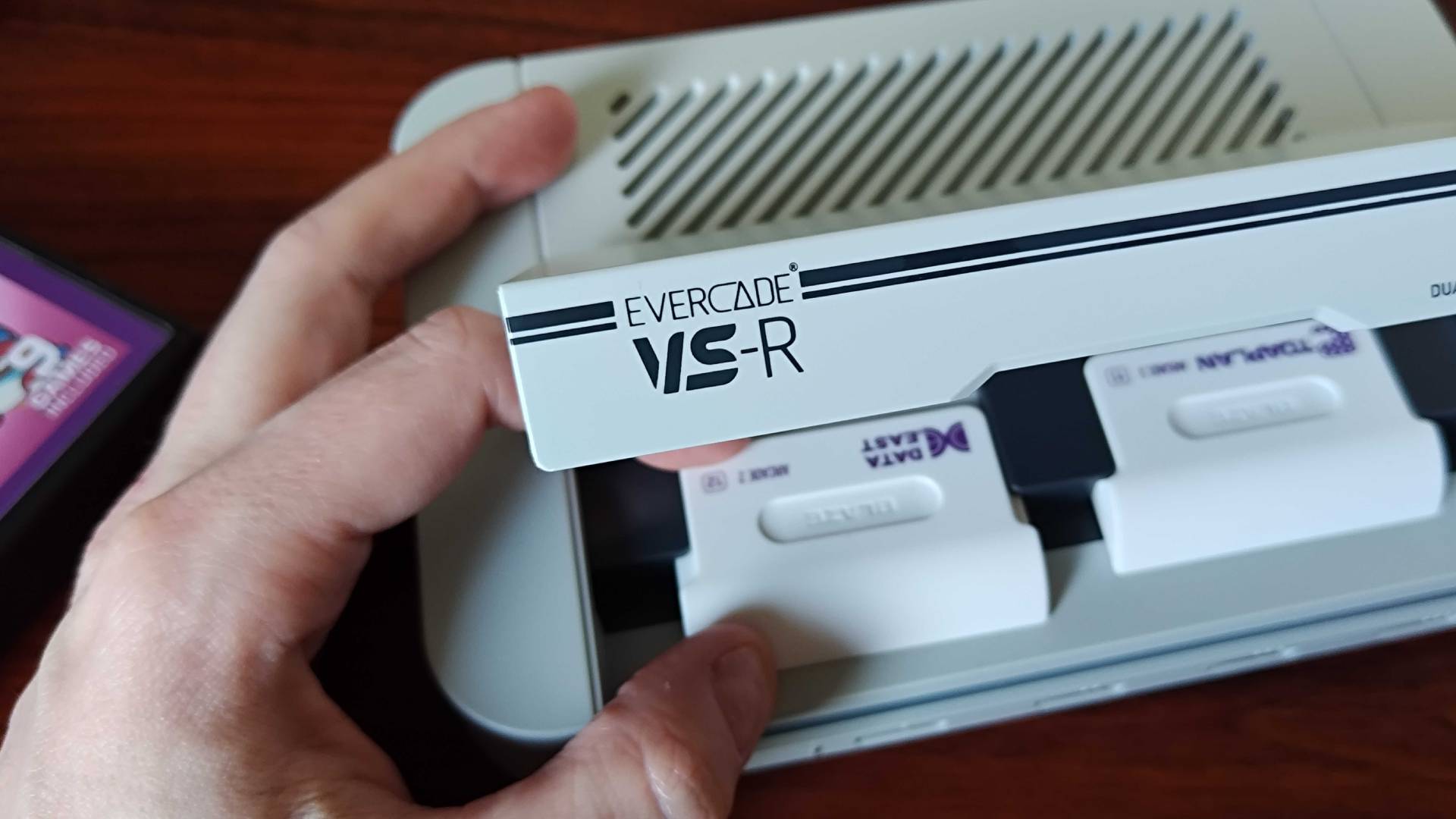 Close up of Evercade VS-R console with front lid open and hand inserting cartridge.