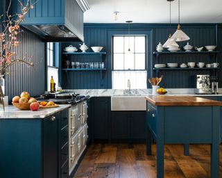 dark blue kitchen with tongue and groove walls and cabinets, blue island, glass pendants and white range cooker
