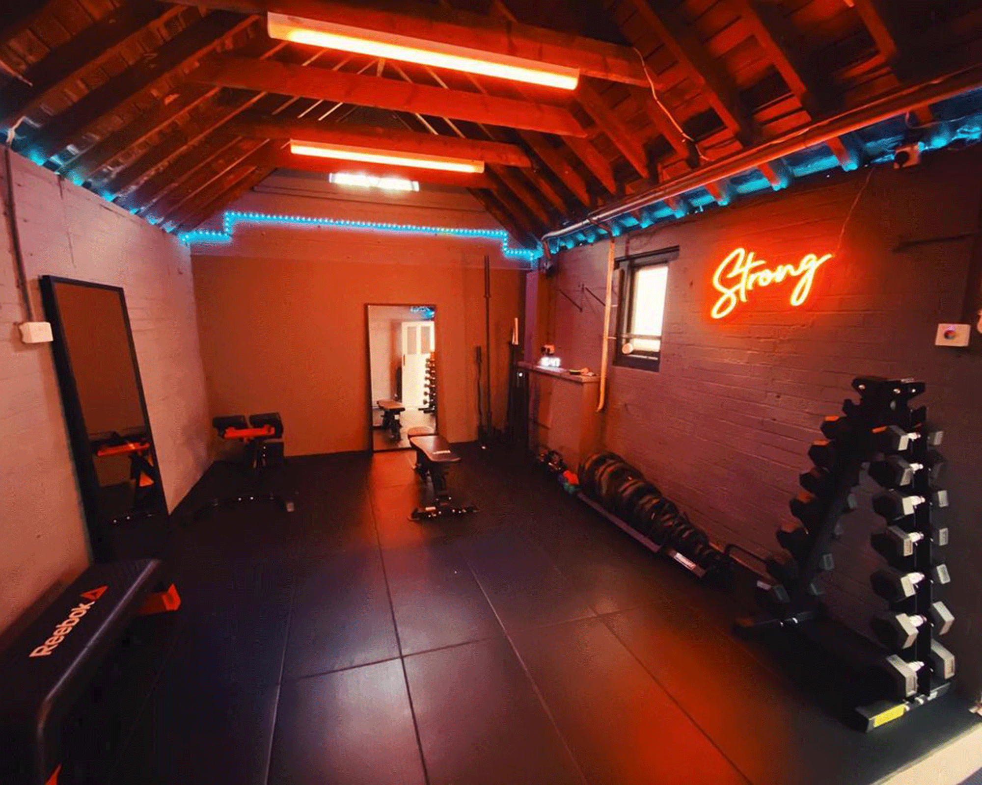 A home gym with red mood lighting and neon 'Strong' light