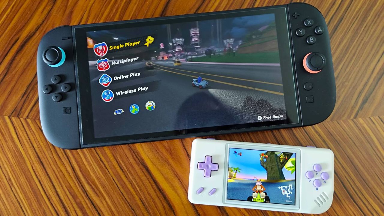 Anbernic RG28XX handheld with Crash Team Racing on screen sitting under Nintendo Switch 2 running Mario Kart World on woodgrain table.