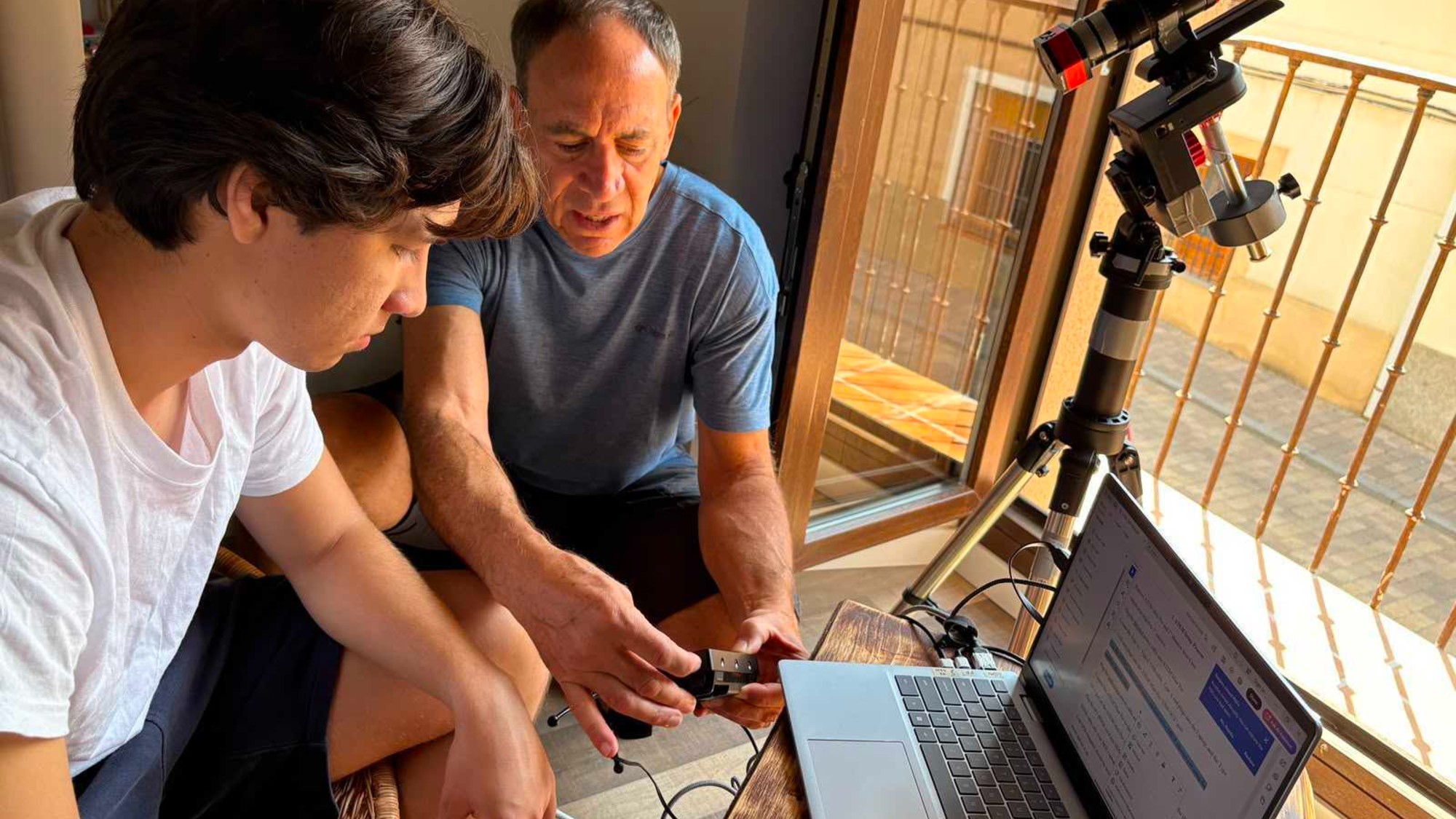 two people look at a laptop computer next to a telescope