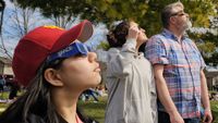 Two girls and a man observe the total solar eclipse of April 8, 2024 with eclipse glasses