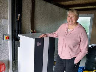 Woman in pink hooded top stood in front of a ground source heat pump in her home