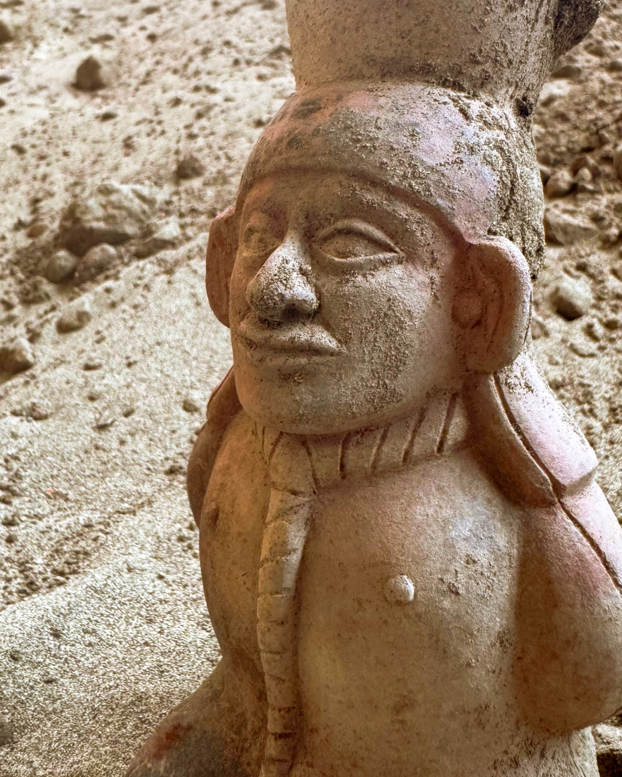 A ceramic statue with a large head and ears sits in a cave.