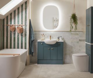 loft conversion bathroom with freestanding bath under sloped roof, narrow green and white tiles laid in vertical pattern on eaves walls, large floor tiles and narrow paler tiles run horizontally on lower section of remaining walls