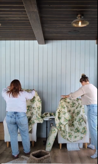 Two women covering two arm chairs with floral patterned slip covers