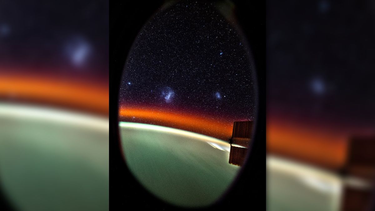 through an oval window, thousands of stars and several wispy clouds of light can be seen above a round, green blur of light with a thin red upper layer