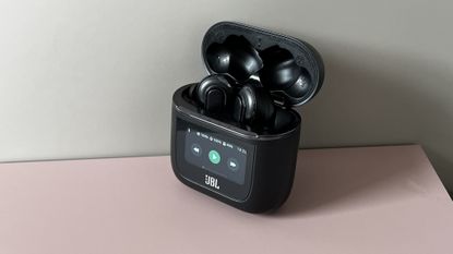 The JBL Tour Pro 2 earbuds on a pink and grey background