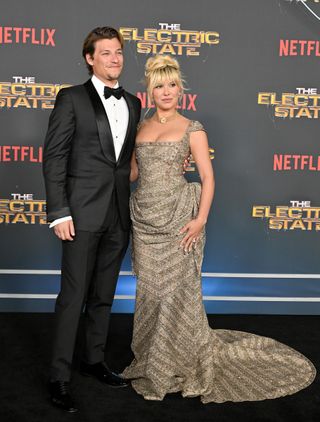 A photo of Brown posing in a gold cap-sleeved Annie's Ibiza gown and a gold choker with her husband Jake Bongiovi.