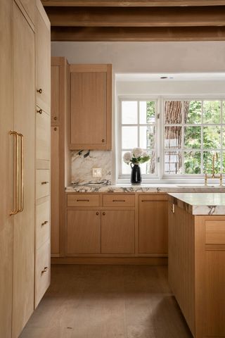 A kitchen with light wooden floors, and wooden cabinets with chrome handles