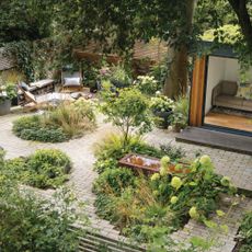  Birds eye view of the garden with a garden room, patio seating area, water feature and borders of green shrubs. Pub Orig Karen Howden and Tom Gandey's ground floor flat's garden in North London.