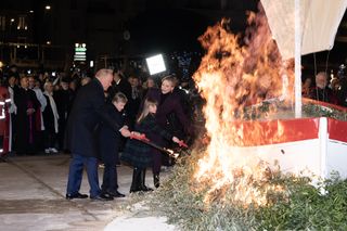 Prince Albert, Prince Jacques, Princess Gabriella and Princess Charlene wearing coats and lighting up a wooden boat on fire with lighters