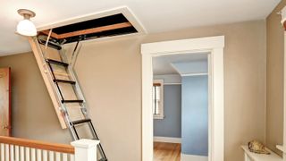 Open rectangular loft hatch with built in ladder against a beige wall with wooden bannisters and flooring