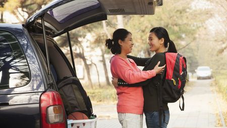 A mom and daughter hug outside their SUV as the daughter prepares to go away to college.