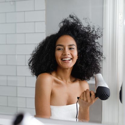Smiling Young Woman Drying Hair Reflecting On Mirror - stock photo