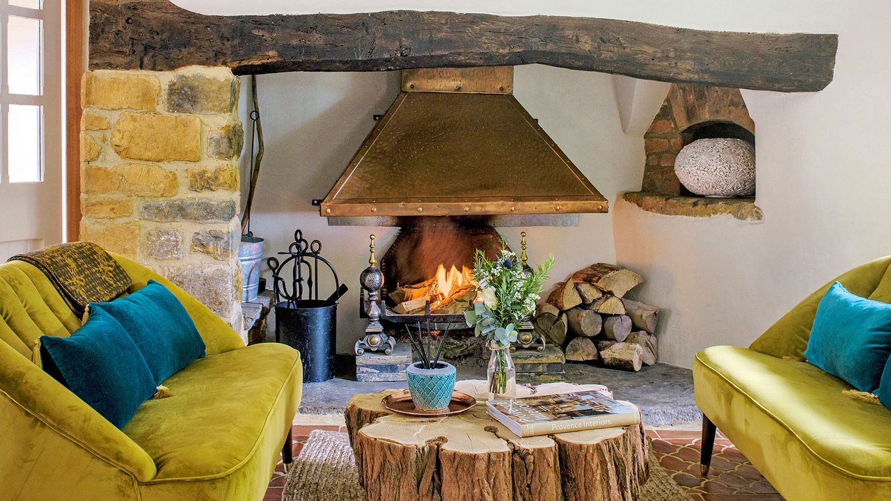 Living room with tiled floor, lit fire in inglenook fireplace, lime sofas either side of wood trunk coffee table.