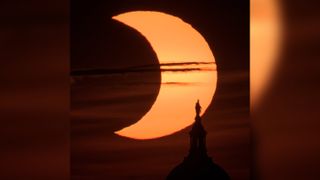 A partial solar eclipse is seen as the sun rises behind the Statue of Freedom atop the United States Capitol Building, Thursday, June 10, 2021, as seen from Arlington, Virginia.