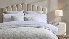 A neutral, beige, bed with textured, cream bedding from Dusk in a modern, minimalist bedroom.