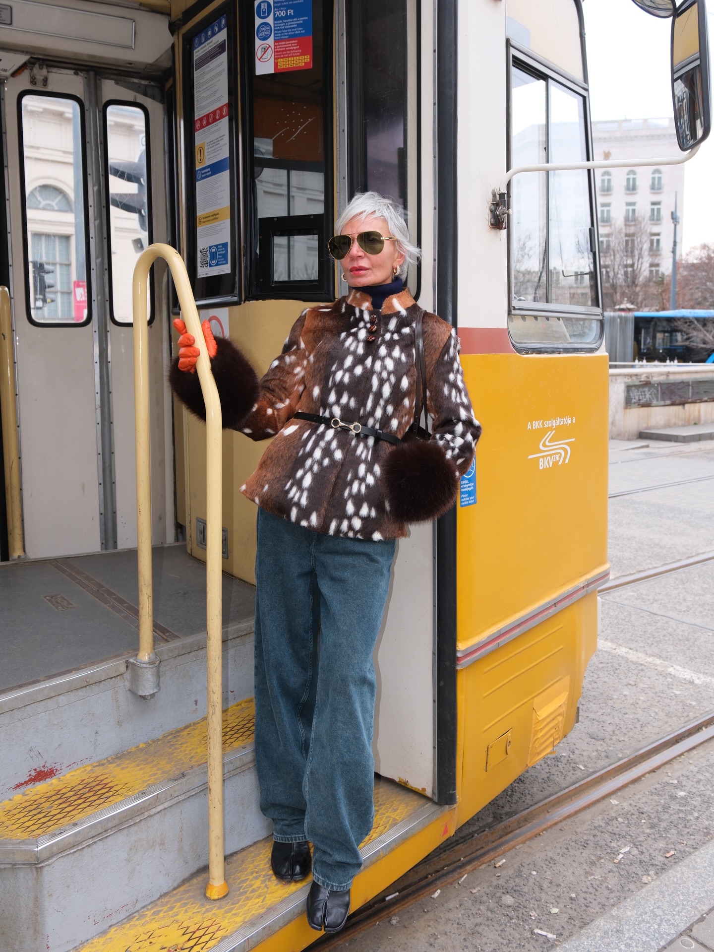 woman posing holding onto a bus in a pair of jeans, jackets, and flats