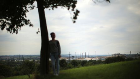 Young woman in shadows standing under a tree with cityscape behind her