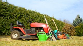 Red riding lawn mower on grass with other gardening tools
