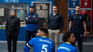 From left to right: Nate, Beard, Ted and Roy all standing together in front of the team in the locker room on Ted Lasso.
