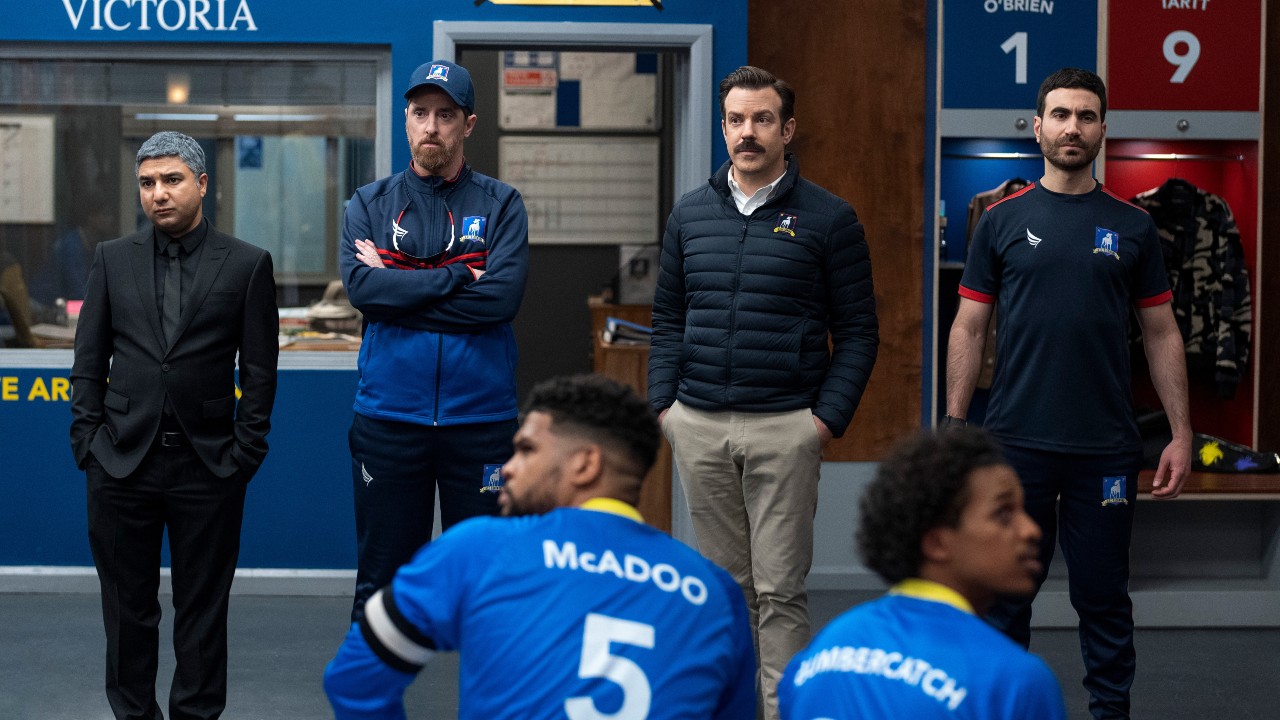 From left to right: Nate, Beard, Ted and Roy all standing together in front of the team in the locker room on Ted Lasso.