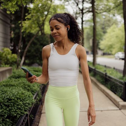 A woman walking on the street in white and green activewear, aiming for 7000 steps a day