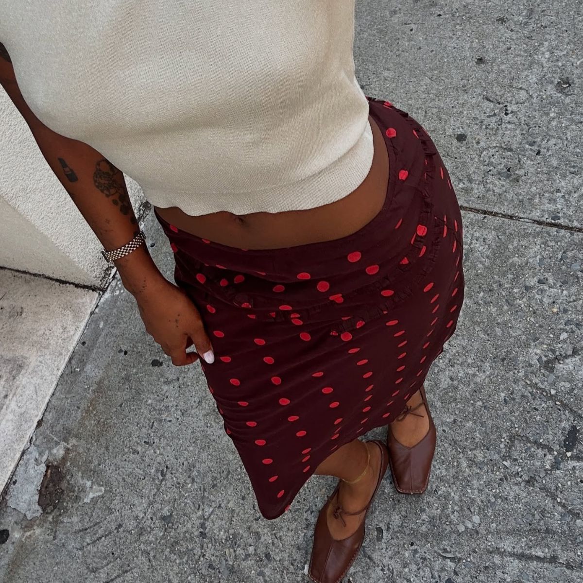 Woman wears cream top, polka dot skirt and burgundy loafers