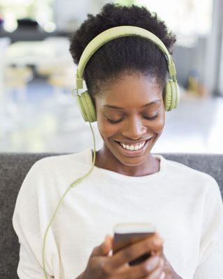 A woman wearing headphones smiles as she looks at her phone screen
