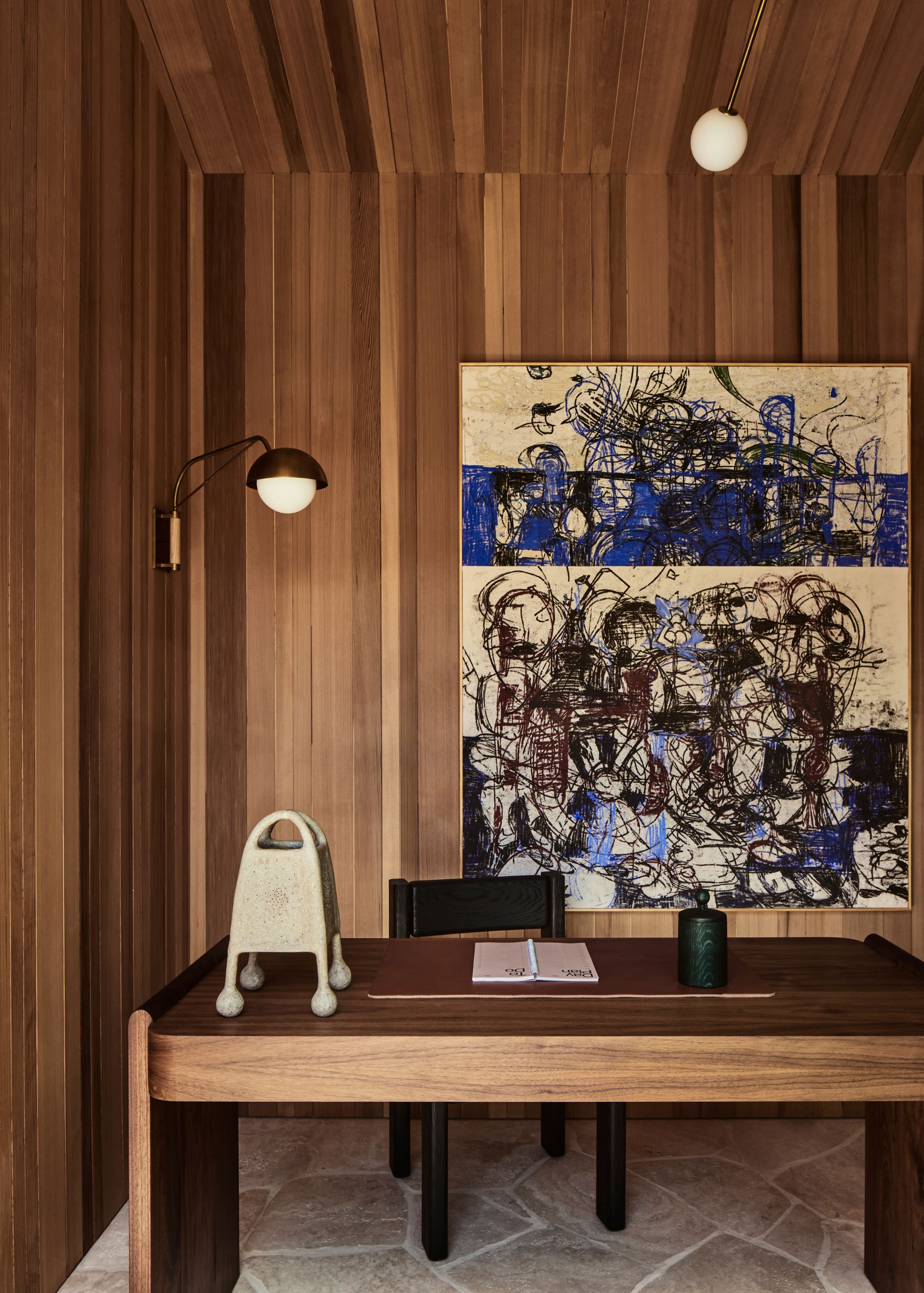 A modern wood-clad home office with a large wooden desk and abstract artwork on the wall.