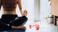 Does yoga help you lose weight? Image of a woman sitting on a yoga mat with a dumbbell next to her