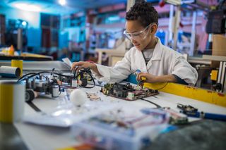 Smiling boy with safety glasses works on circuit board.