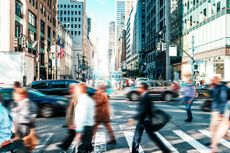 Blurred office workers cross a busy street in New York City.