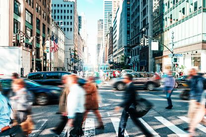 Blurred office workers cross a busy street in New York City.