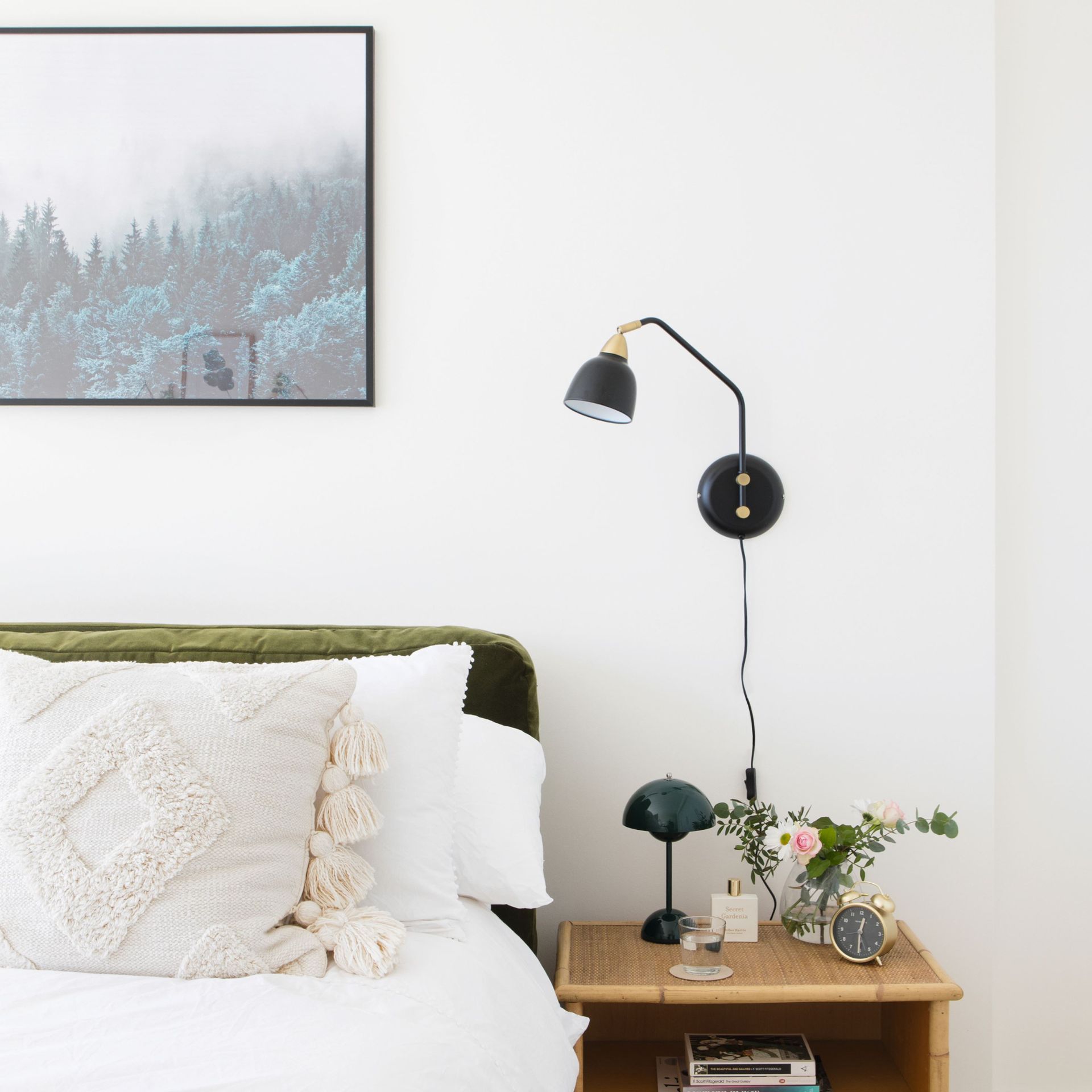 Tempat tidur dengan seprai dan bantal selimut putih, meja samping tempat tidur rotan dengan lampu, hiasan dinding gantung di kamar tidur bercat putih