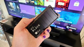 WD_BLACK P40 Game Drive SSD for Xbox and PC, shown in hand in front of Xbox Series X setup..