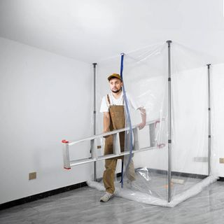 Man exiting clear plastic sheeting with metal poles surrounding renovation work area