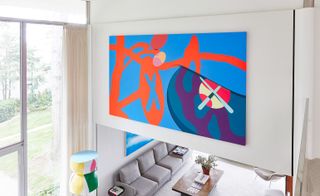 Brightly coloured art work on a living room wall next to floor to ceiling windows with cream curtains