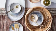 Tablescape with pale blue crockery, gold cutlery, and a wicker serving basket