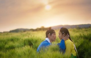 a couple wearing joseon-era historical costumes are about to kiss while sitting in a field, in a still from the k-drama 'my dearest'