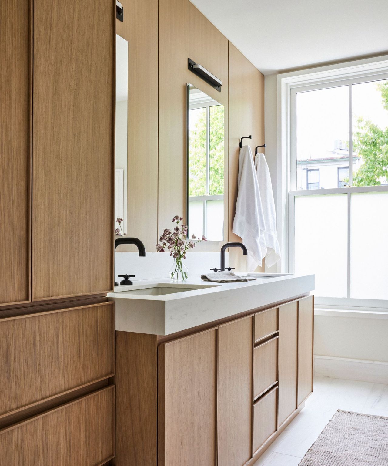 A bathroom with wooden cabinetry, a white sink, and a large window