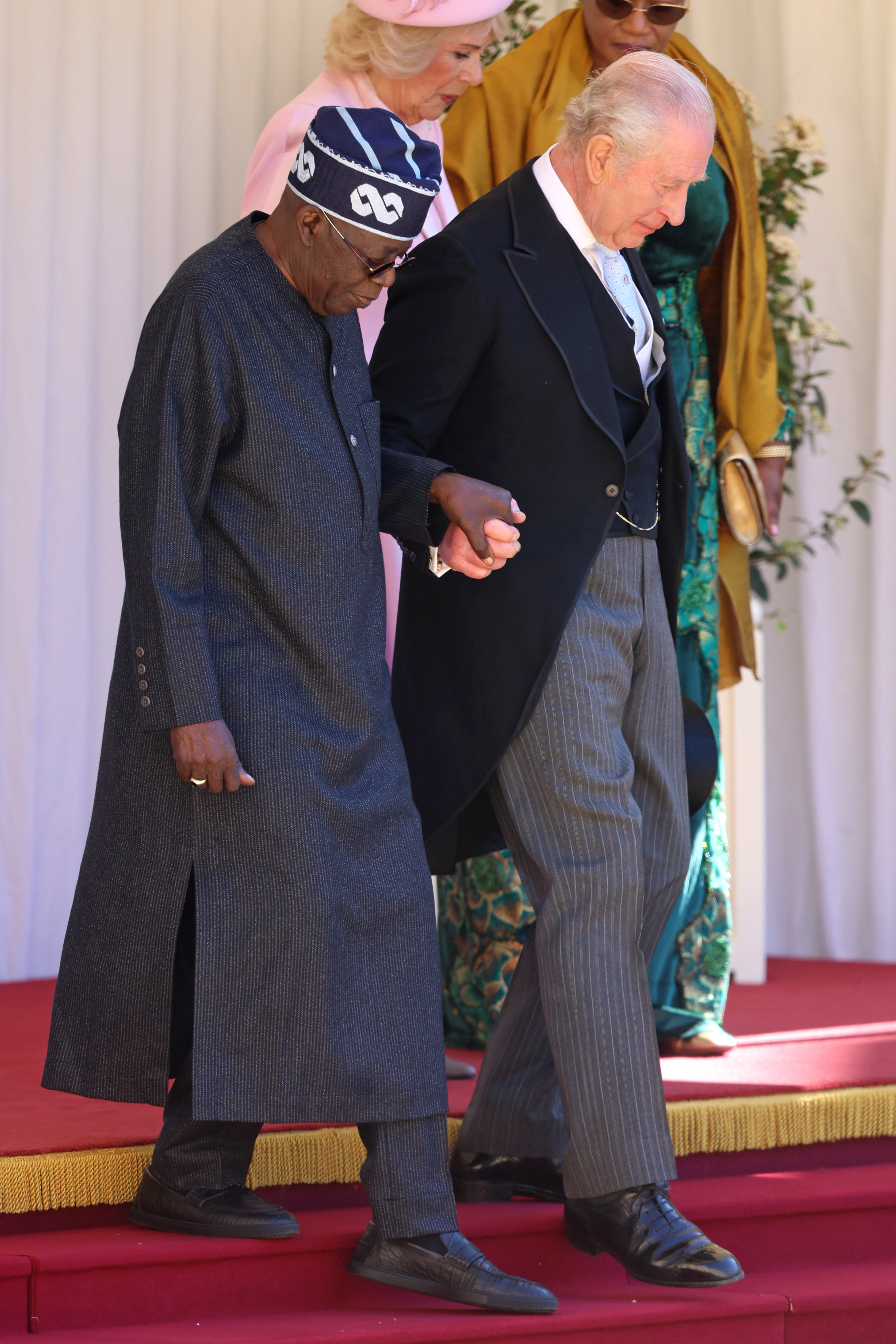 WINDSOR, ENGLAND - MARCH 18: President of the Federal Republic of Nigeria Bola Ahmed Tinubu and King Charles III hold hands in the Quadrangle at the inspection of the Guard of Honour during a ceremonial welcome at Windsor Castle on the first day of State Visit by The President of the Federal Republic of Nigeria on March 18, 2026 in Windsor, England. President Bola Tinubu and First Lady Oluremi Tinubu are conducting a historic State Visit to the United Kingdom, marking the first state visit by a Nigerian leader in 37 years and the first to be hosted at Windsor Castle. (Photo by Chris Jackson/Getty Images)