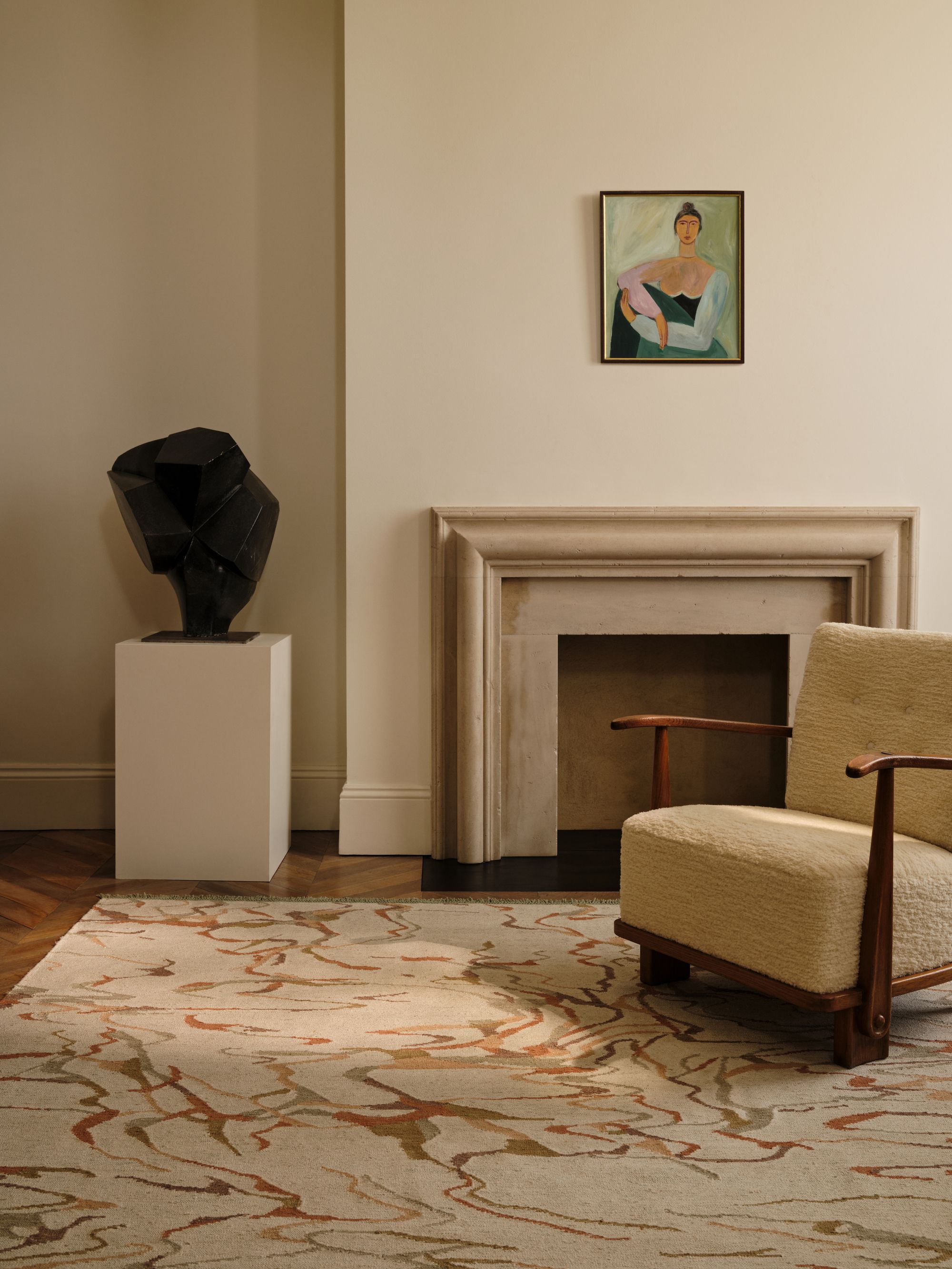 Image of a beige living room with a beige, red, and sage marble design rug. There is a stone fireplace, a butter yellow accent chair, and a black sculptural art piece.