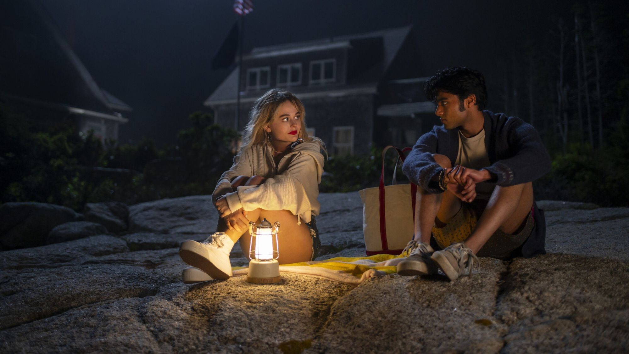 Emily Alyn Lind and Shubham Maheshwari sitting on rocks at night in We Were Liars