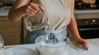 A woman pouring water from a measuring jug into a mixing bowl