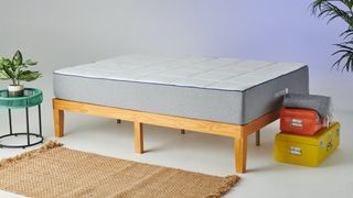 The Nectar Mattress placed on a light wooden bed frame with an orange metal suitcase at the end